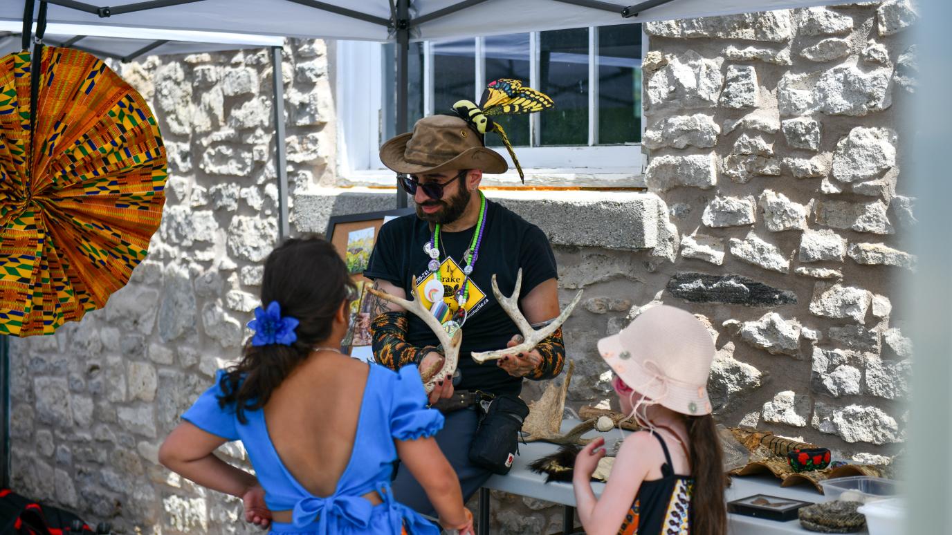 A performer at the 2025 Multicultural Festival speaks to two children while holding a pair of antlers.
