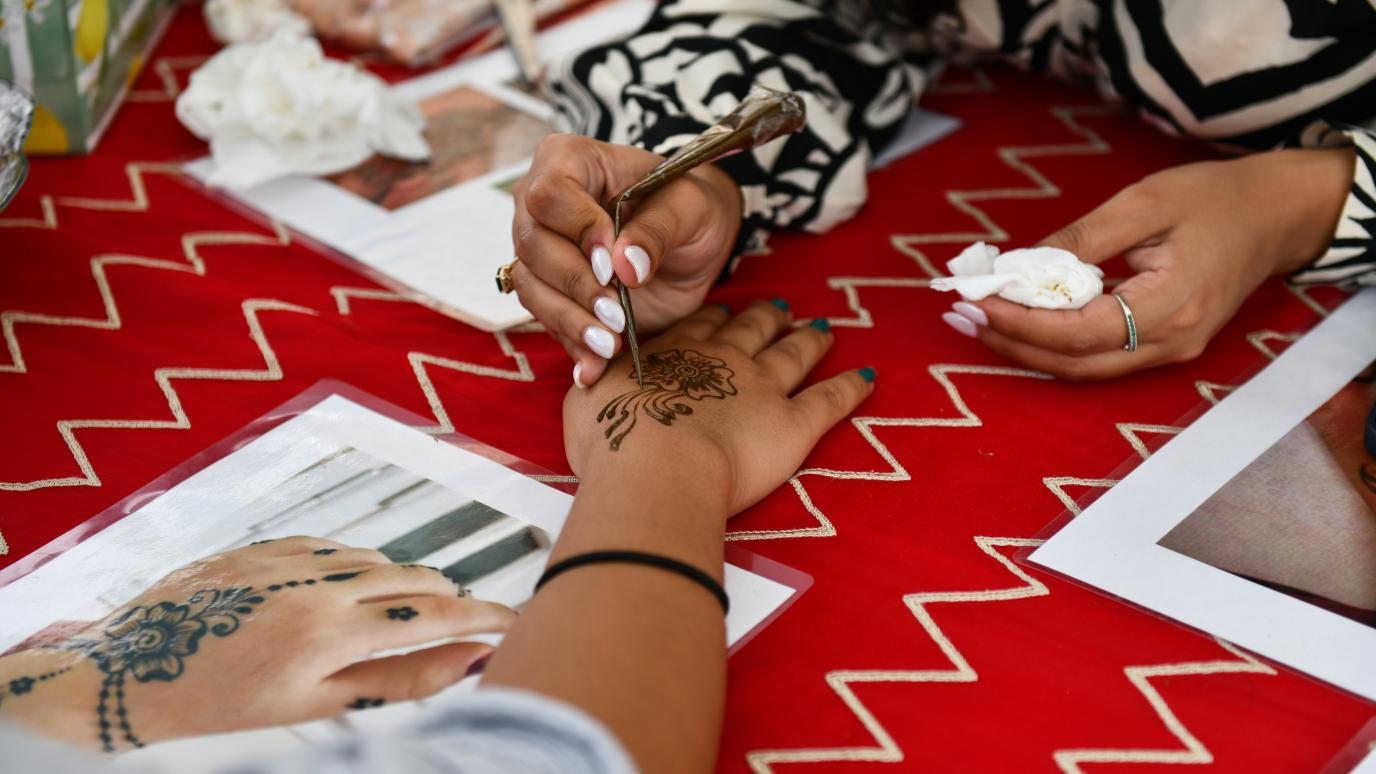 A person has their hand painted with brown henna atop a red tablecloth.