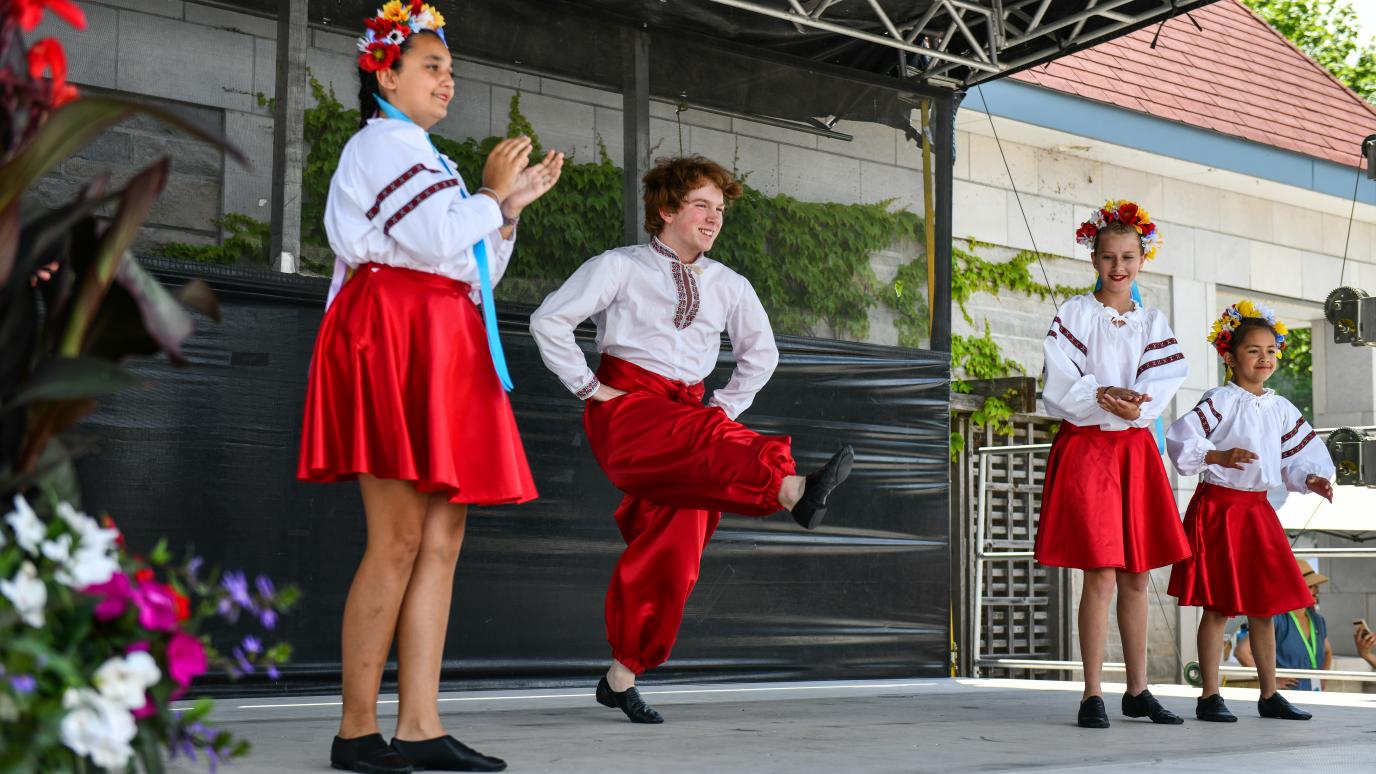 A group in matching white shirts and red bottoms claps and dances on stage at the 2025 Multicultural Festival.