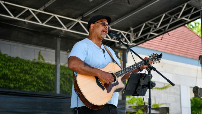 Man in a blue shirt playing an acoustic guitar on the outdoor stage at the Multicultural Festival.