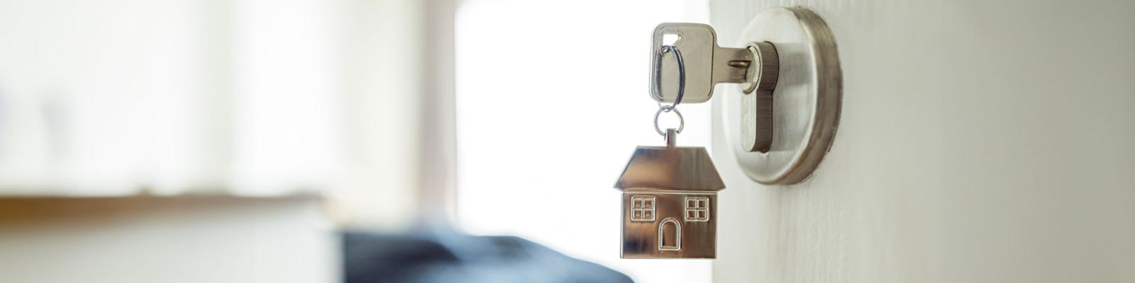 Key in door with a silver keychain shaped like a house