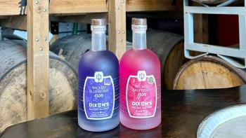 A colourful purple and pink gin bottles sit on a table with casks of gin in the backgroun