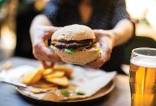 Outstretched hands reach to show off a burger across the table at a restaurant