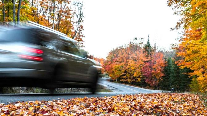 Speeding car down a rural road in the Autumn stirring up leaves as it rounds a corner