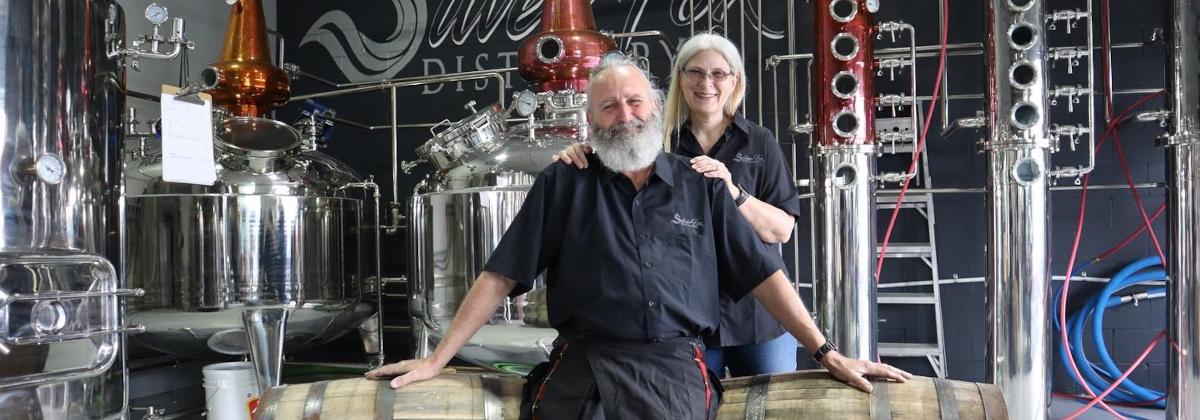 two people sitting on barrels beside distilling equipment