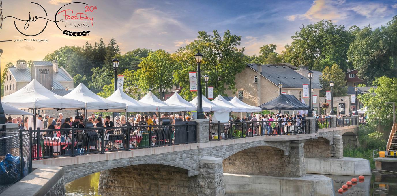 A wide-angle shot of the pedestrian bridge in Elora, which is lined with white tents and people crossing the bridge